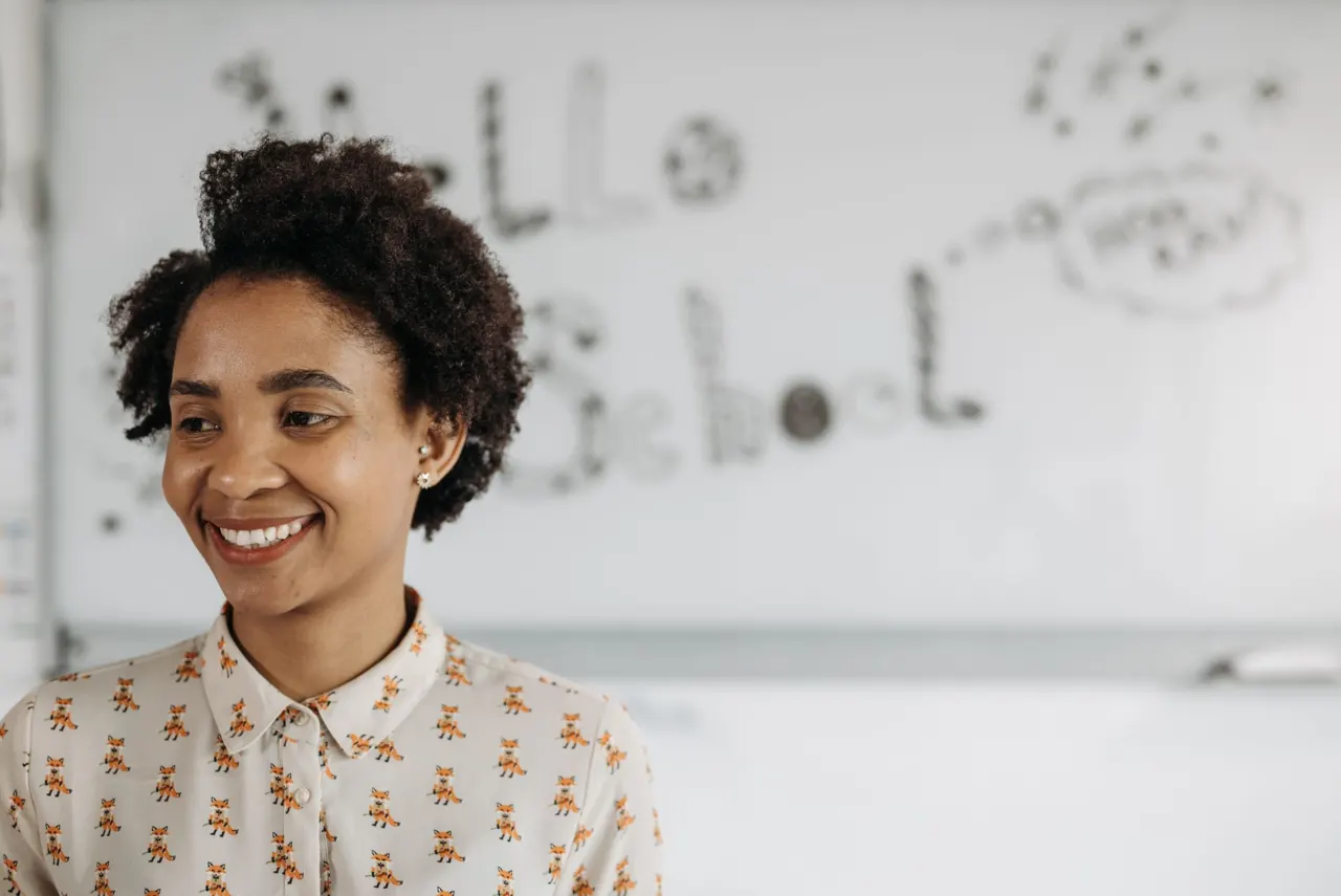 A smiling teacher in front of a classroom whiteboard