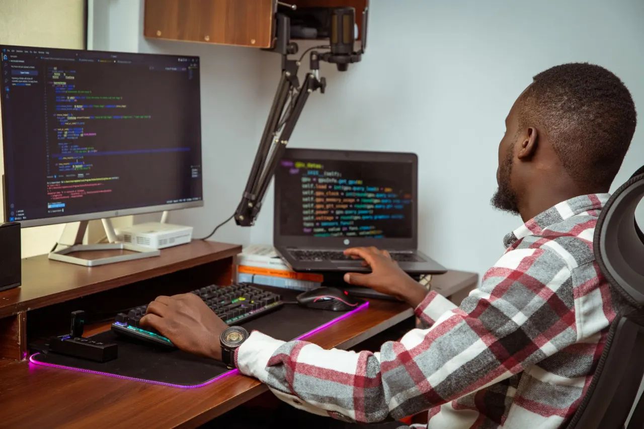 A developer writing code at a desk with two screens